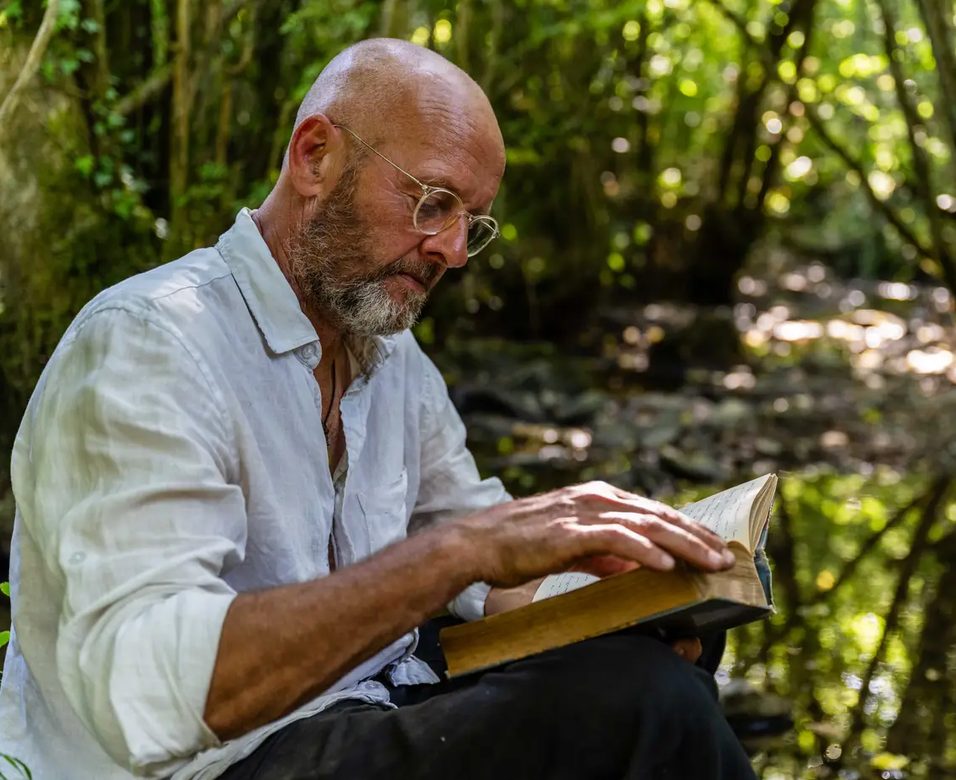 Alain lit, assis au bord du ruisseau